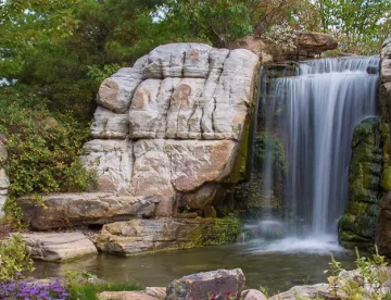 Swimming pool waterfall with surrounding rocks and vegetation.